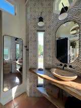 The bathroom has natural edge Hawaiian mango wood slabs spanning the length of the bump-out: the vanity countertop and the shelf beneath. The entire bump-out-side wall is tiled floor to ceiling with a diamond print pattern. The shower follows the high contrast trend with one white wall and one black wall in matching square pearl finish. The warmth of the terra cotta floor adds earthy warmth that gives life to the wood. 3 wall lights hang down illuminating the vanity, though durning the day, you likely wont need it with the natural light shining in from two perfect angled long windows.  