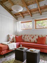 Original pine wall boards are painted white to reflect light in the den. A George Nelson pendant hangs above a clean-lined sectional sofa atop carpet tiles by FLOR. The pillows are made from MissPrint Garden City fabric, and the quilt is from Haptic Lab.