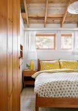 The existing pine wall boards in the guest bedroom are painted white to reflect light. The windows look east. The furniture is from Room & Board, and the pendant light is by George Nelson. The pillows and duvet are made from fabric by MissPrint.