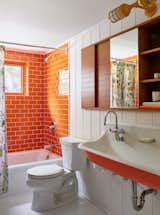 The kids’ bath has a whole new look that includes orange glass subway tiles by Ann Sacks, ceramic penny tile, an orange trough sink, and sconces from Barn Light Company. The custom recessed medicine chest is made from mahogany with a butternut-colored finish.