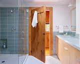 Sutherland added a skylight to new primary bath, which is located behind the couple’s bedroom. The custom maple vanity has a white concrete top and Kohler Purist fixtures. The glass Roku wall tile in Rain Gloss is by Walter Zanger, and the ceramic floor tile is Original Style Moonbeam penny round. The new door is a copy of the cabin’s original interior doors. “I love how the wood door plays against the modern tile,” Sutherland says.