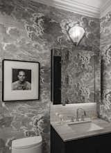 In the bath, a portrait of English actor Joseph Fiennes by Herb Ritts hangs atop existing Cole & Son "Nuvolette" wallpaper by Piero Fornasetti, and the Gabriel Scott sconce relates to the chandelier in the dining room. O'Donnell added crown molding and designed a new vanity in the same style as the media console and new kitchen cabinet doors.