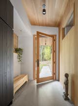 In the entry, a high interior window borrows light from the bedroom wing and a woven wood screen in the kitchen lets the owners see who’s at the front door. Kalon Studios crafted the bench from a single ash log. “It will split a bit over time,” Lachapelle says. 