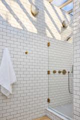 White subway tile with charcoal-colored grout covers the primary bath where sunlight streams in from overhead thanks to a huge, new skylight. Wall sconces from The Urban Electric Co. lend a nautical feel.
