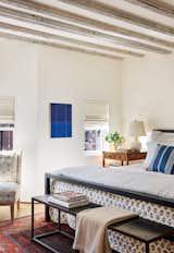 The primary bedroom has small windows but lofty ceilings with original exposed beams. The comforter is from Out of Hand in G<span style="font-family: Theinhardt, -apple-system, BlinkMacSystemFont, &quot;Segoe UI&quot;, Roboto, Oxygen-Sans, Ubuntu, Cantarell, &quot;Helvetica Neue&quot;, sans-serif;">reat Barrington</span><span style="font-family: Theinhardt, -apple-system, BlinkMacSystemFont, &quot;Segoe UI&quot;, Roboto, Oxygen-Sans, Ubuntu, Cantarell, &quot;Helvetica Neue&quot;, sans-serif;"> , Massachusetts, the table lamp is by Christopher Spitzmiller, and the vintage rug came from a dealer in Cleveland . With her daughter's help, Priscilla carried the (</span><span style="font-family: Theinhardt, -apple-system, BlinkMacSystemFont, &quot;Segoe UI&quot;, Roboto, Oxygen-Sans, Ubuntu, Cantarell, &quot;Helvetica Neue&quot;, sans-serif;">since reupholstered) </span><span style="font-family: Theinhardt, -apple-system, BlinkMacSystemFont, &quot;Segoe UI&quot;, Roboto, Oxygen-Sans, Ubuntu, Cantarell, &quot;Helvetica Neue&quot;, sans-serif;">Jonathan Adler chair home from his shop on Atlantic Avenue. "The store was closing, so the chair was so cheap that having it delivered would have cost more than the chair itself,