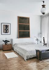 The upcycled Tasha ORO Solar lamp made from the remains from the Soviet car industry echoes the shapes in the Olga Fradina print in the primary bedroom. A hemp fur throw by DevoHome covers the bed a rustic Swiss cradle is a storage spot for books and magazines.