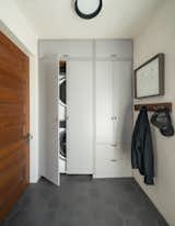 The entry is full of function, including a washer/dryer that hides behind a mod arrangement of floor-to-ceiling cabinetry made from painted MDF with walnut detailing.