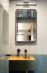 Penny tiles in two colors cover the walls in the wet room on the second floor where wall-mounted plumbing fixtures preserve countertop space atop the solid brass sink.