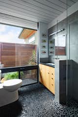 A glass wall and flooring that continues from inside to out, creates the experience of an outdoor bathroom.