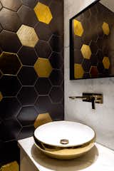 A large apartment in the Indian city of Mumbai features a range of materials, textures and patterns throughout the spaces, and the powder room is no different, with hexagonal tiles on the walls and a marble vanity that serves as the support for a gold and white vessel sink.
