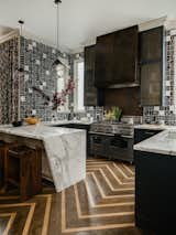 Black & white geometric tiles paired with a custom a range hood and cabinetry in burnished metals are just a few of the features of the energetic, modern kitchen.