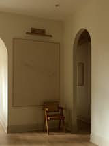 A Hinkley picture light from Lightology illuminates a plaster painting by Qing Liu and an RH chair.