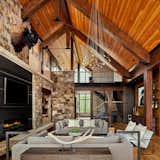 A stone wall holds the fireplace and acts as a grounding element, balancing the floor-to-ceiling windows.