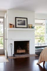 Painted white, screen removed, and decorated with just a few pieces of art, the brick fireplace looks fresh, and acts as the perfect textural foil to the glossy floors and the leafy view beyond. A photograph by Wayne Levin and a small painting by Peter Shepard Cole create a thoughtful vignette on the mantel.