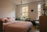 The rosy glow reflecting off maple leaves and the brick of neighboring homes inspired Maureen to choose the blush pink bedding. The soft linen bedding, from Hawkins New York, along with the minimal decor, the calming natural green of the plants, and the warm wood furniture combine to make the room an inviting, spa-like space.   Photo 5 of 6 in Bedroom by Jinny J from My House: A Brooklyn Couple’s 1800s Townhome Melds Eras, Heirlooms, and Artwork