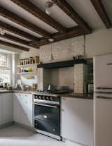 While renovating the kitchen, the couple uncovered the original wooden beams and brick hearth. To emphasize its European style, they installed a Lacanche French range and open shelving.