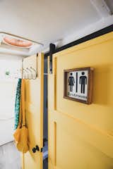 A split bathroom allows the sink to be easily accessible in the main living area of the school bus, and a toilet and shower are tucked behind a yellow barn door.