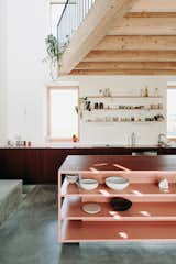 The living spaces center around the kitchen, where a custom-built island in salmon pink stands out.