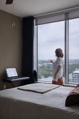 Architect Guta Louro stands behind her bed and next to a piano looking out at the views over Lady Bird Lake. 