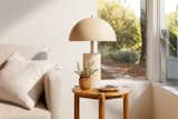 A lamp with a mushroom shade sits on a mid-century end table next to a couch. 