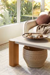 A coffee table with oak legs and travertine top sits in front of a couch. A woven basket is placed beneath the coffee table. 
