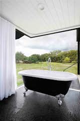 In the en suite, a black Victoria + Albert tub (with matching black American Universal penny tile) makes the perfect spot to soak up the view—though the shower curtains that line the windows can be drawn for a little more privacy. A shower head is mounted off to the right. 