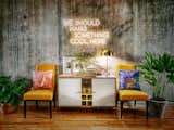 A formal buffet-and-side-chair configuration against an exposed concrete wall is the juxtaposition that defines the overall style of this unit. Custom neon sign adds a playful touch.