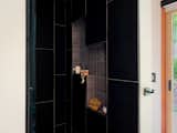 Detail of the shower with black stone tiles in a running bond pattern with a gray stone tile inlay to create two functional niches. 