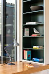 In the office, a custom-designed desk seamlessly integrates with a vibrant bookcase, infusing the space with color and meticulous attention to minimalistic details.