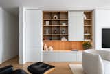 The custom wall-to-wall millwork anchors the living room, balancing light-toned cabinetry, natural oak, and black metal accents. At its center, a recessed niche frames the TV, while a discreet frameless door provides access to the apartment’s private quarters.