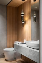 In the powder room, cool tones of plaster and stone are complemented by the warmth of wood, creating a balanced and inviting contrast.