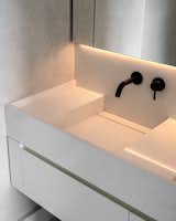 A close-up of the custom integrated sink and vanity in the primary bathroom, complemented by black plumbing fixtures and softly textured plaster walls.