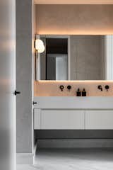 A front view of the wall-to-wall custom integrated sink and vanity  in the primary bathroom. The medicine cabinets are seamlessly integrated with a continuous mirror, framed by hidden linear lights above and below to highlight the soft texture of the plaster walls.