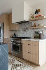 Kitchen, Light Hardwood Floor, Range Hood, Range, Wood Cabinet, Stone Slab Backsplashe, and Marble Counter  Photo 6 of 15 in Ocean Views For Days by Katie Betyar