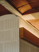 The prefabricated concrete half-joists rest on a thermo-clay wall that encloses the courtyard and supports the ceramic vaults from the roof. Here, a custom-designed piece of wood holds an indirect light.