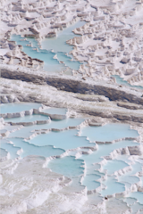 The terraced travertine pools of Pamukkale sit in the southwest Denizli region of Turkey, carrying with them the ancient history of a holy city where emperors soaked and, it’s rumored, Cleopatra swam. "Bathing is one of the many practices of letting go," says Ekin Balcıog˘ lu of Hamam magazine. In Turkish culture and around the world, "bathing can be communal or personal," and on some level, it’s always profound. Pamukkale’s seventeen pools sit above the Anatolian Plateau, featuring shallow thermal waters that range from 91 to 212 degrees Fahrenheit. Heated by subterranean tectonic activity, the water pushes its way through 984 feet of earth, including a layer of limestone that dissolves into the liquid, enriching the bicarbonate and colloidal-iron water with calcium carbonate. As the water evaporates, the calcium carbonate is left behind, creating a gel that eventually petrifies to form travertine, which gives the terraces their iconic white features. This explains the name Pamukkale, which translates to "cotton castle."