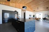 Charcoal custom kitchen with custom cabinetry, waterfall center island, black pendant lighting, wood clad soaring 15' vaulted ceilings and matte black kitchen faucet
