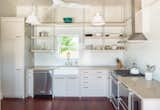 The kitchen opens to a farmhouse sink, custom Millwork with hanging shelves, under counter refrigerator, and white stone wall panels.