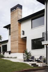 Rough wood siding on chimney and sitting area in front of home.