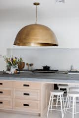 Kitchen, Wood Cabinet, Light Hardwood Floor, Ceiling Lighting, Stone Slab Backsplashe, Range, and Stone Counter A brass dome pendant statement is the perfect balance to the large island and simple range wall layout.  Photo 5 of 25 in The Gernert Home by Jamie Gernert