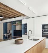 Kitchen, Undermount Sink, Marble Counter, Microwave, Wall Oven, White Cabinet, Wood Cabinet, Light Hardwood Floor, Refrigerator, and Ceiling Lighting view to TV and office space from the kitchen  Photo 1 of 13 in Can Albert by Domuslabs