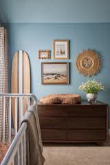 A simple walnut dresser acts as the changing table under a collection of vintage beach paintings. 