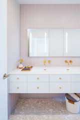 The bathroom walls and shower stall are lined with pink glass tile from Fireclay, while the terrazzo tiles on the floor are from Ann Sacks. The brass fixtures are by Graff.  The medicine cabinets are from Robern.