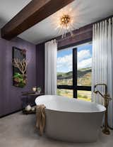 This organically shaped freestanding tub sits in front of a window, showing off the magnificent view. A crystal flush mount light, paired with sheer drapery panels and a brushed gold tub filler give this space some major ambiance!