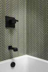 This guest bath features a grey glass mosaic herringbone tile with lime green glitter grout and matte black fixtures!