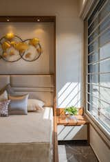 Guest Bedroom is rendered with an off-white color scheme with wooden highlights, inviting the east light, creating the room bright and young. A simple wooden framed niche behind the bed makes the bedroom simply elegant that presents a striking statement with golden accents.
