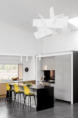 The home's contemporary kitchen features two styles of cabinetry (high gloss gray and whitewashed oak; both by Downsview) and two countertop materials (durable white corian and black granite). Mustard yellow counter stools by Calligaris add a jolt energy to the space.