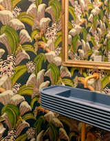 The powder room is wrapped in Cole & Son’s Hoopoe Leaves wallpaper. A curved, Art Deco–inspired concrete trough sink by Kast is the centerpiece.