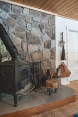 A wood stool with tools on hooks and a basket of birch wood keeps the cabin warm along with a modern furnace in the basement. A small stool made from a log off-cut and hairpin legs functions as both a place to chop down larger logs and sit while stoking the fire.