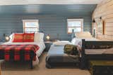 The twin bed frames were originally bunkbeds that were cut. A simple mattress frame with wheels slides under as a perfect fit for a custom trundle bed. The blue wood paneling acts as a continuous headboard, anchoring all the beds against the wall. 